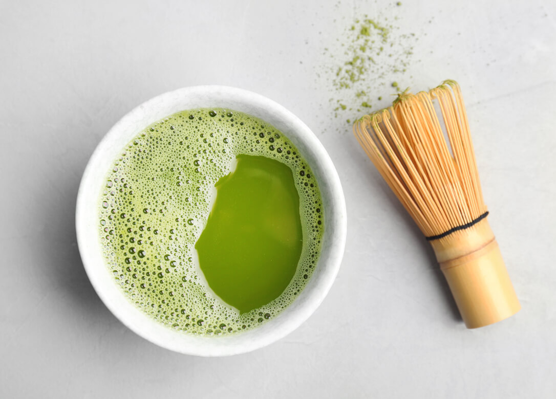 cup of matcha tea and chasen - wooden whisk - on a white background.