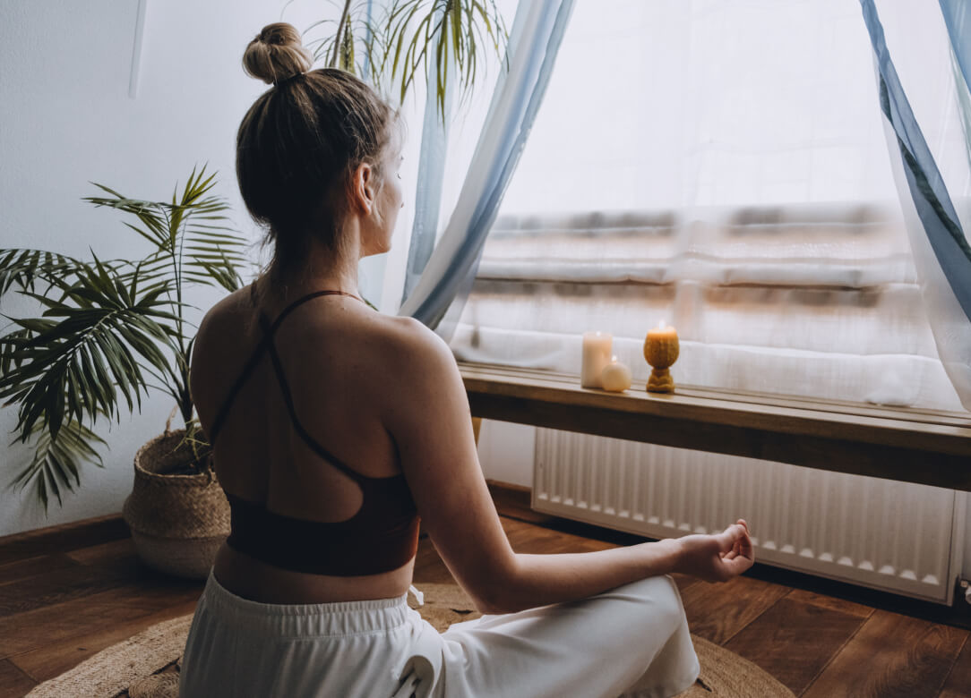 Image of a woman sitting in front of a window in a meditative pose.