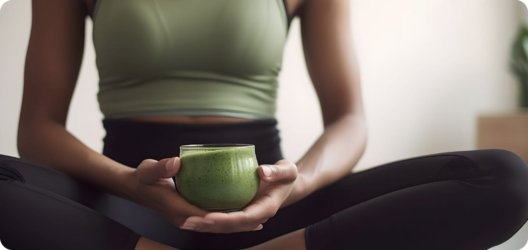 Image of a woman in sports clothes sitting on the floor and holding a cup of matcha.