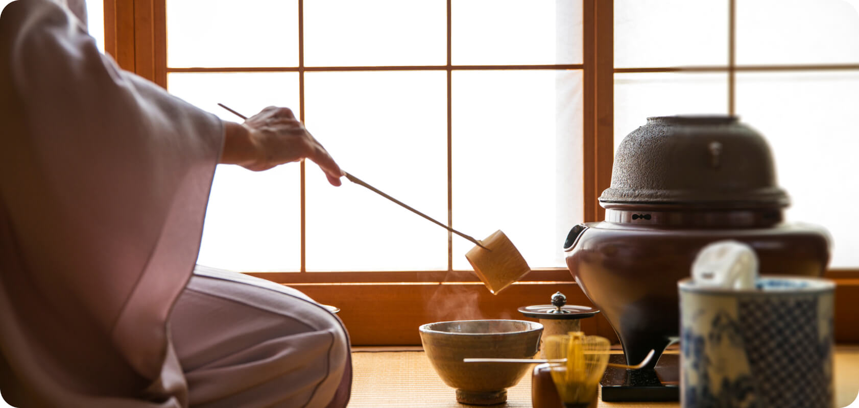 an image of a woman conducting a traditional Japanese tea ceremony. She is sitting on the tatami floor, and using traditional equipment to prepare a cup of matcha.