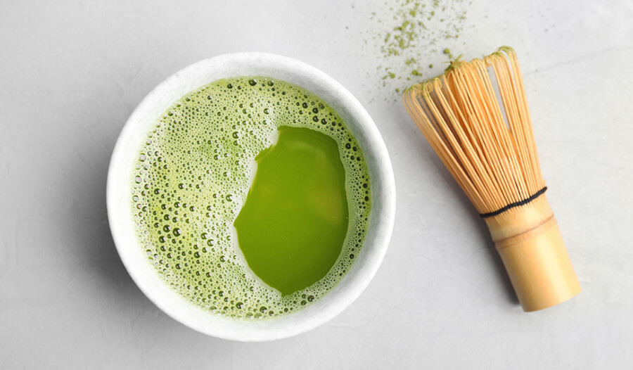 cup of matcha tea and chasen - wooden whisk - on a white background.