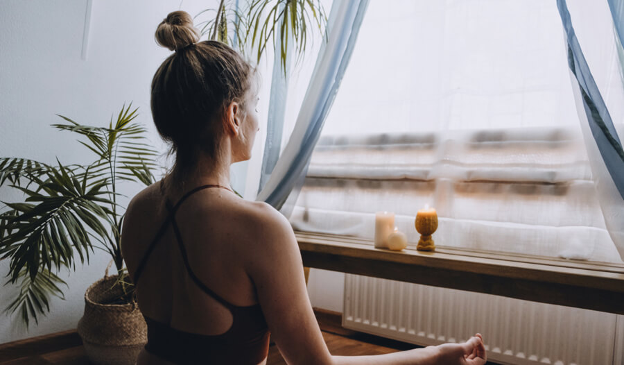 Image of a woman sitting in front of a window in a meditative pose.