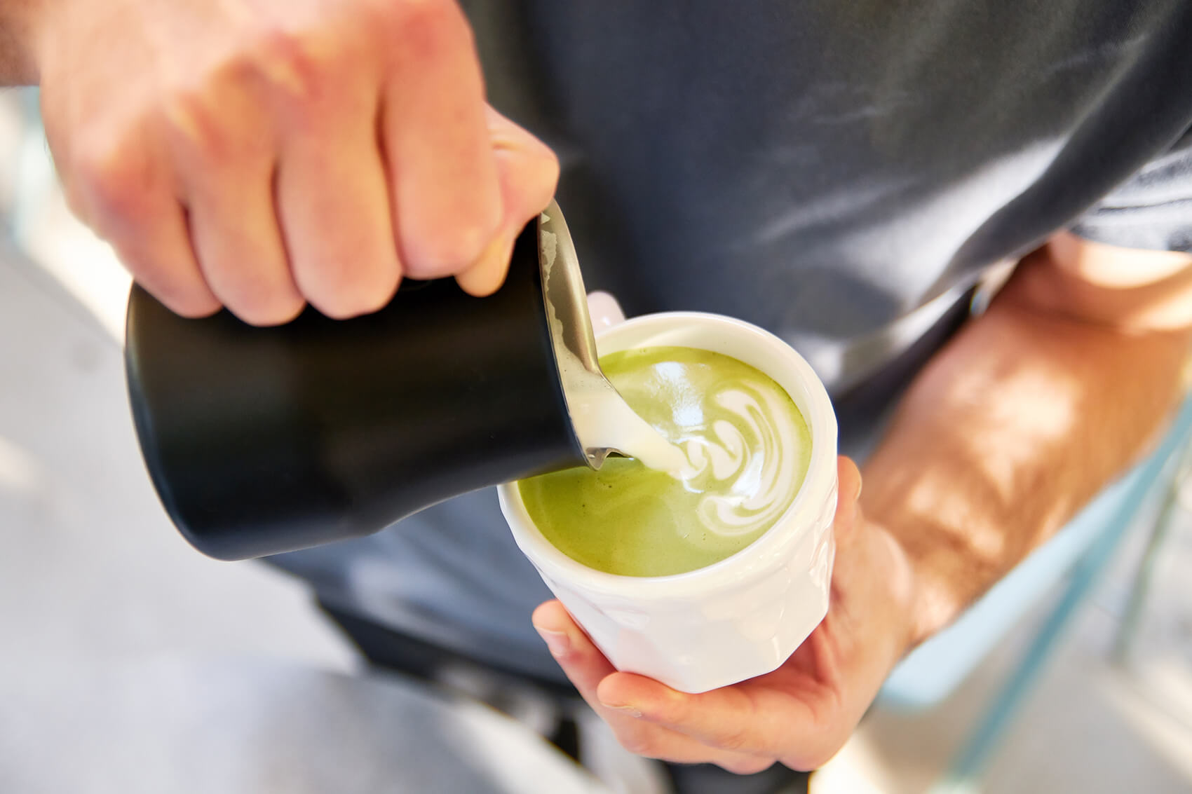 An image of a male barista pouring milk into a cup of matcha latte.